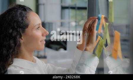 Side view smiling happy successful businesswoman taking notes on stickers writing reminders on color sticky label joyful female project manager Stock Photo