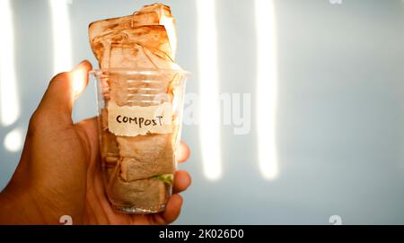 Close up of hand holding plastic drinking glass full of used teabag with text compost written on duct tape Stock Photo