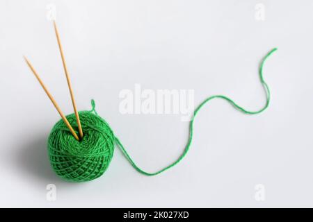 Green yarn thread with knitting needles on a gray background for knitting. Stock Photo