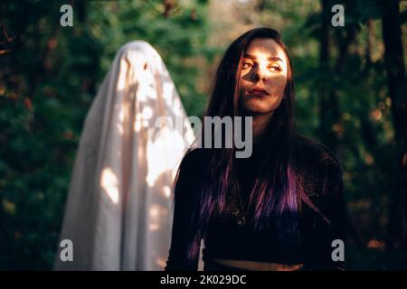 Ghost standing behind young woman in forest during Halloween Stock Photo