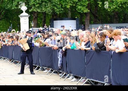 Buckingham Palace, London, UK – Friday 9th September 2022 – A Police officer recieves flowers forwarded by the large crowd outside Buckingham Palace as the public mourn the death of Queen Elizabeth II yesterday. Photo Steven May / Alamy Live News Stock Photo