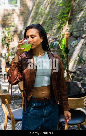 young african american woman in leather jacket drinking green cocktail outside,stock image Stock Photo