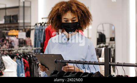 African female shop manager worker girl seller clothing store administrator make inventory salesperson woman in medical face mask owner boutique Stock Photo