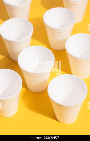 Disposable plastic white glasses on a yellow background in a top view Stock Photo