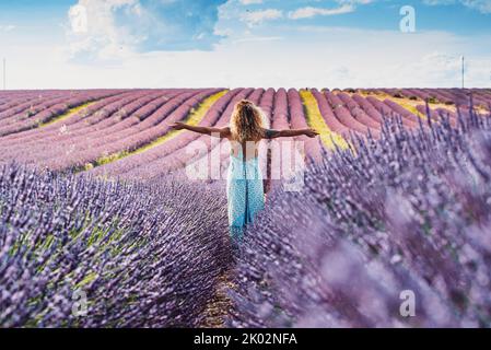 Happy and free traveler woman outstretching arms and enjoy amazing nature landscape in the middle of a violet lavender field flowers scenic destination. Concept of people and travel lifestyle Stock Photo