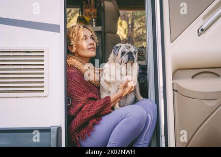 One woman sitting on the camper van door with old nice pug dog looking outside and enjoying relax and freedom. Female people living on a rv motorhome with animals and travel the world. Best friend Stock Photo