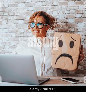 Happy woman take off sad expression carton box from her head after receiving good news on computer. Online successful worker. Female people and victory. Computer job business Stock Photo