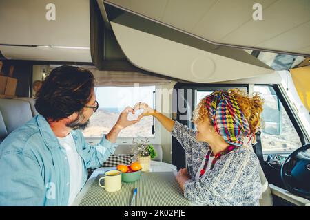 Happy mature couple doing heart gesture sign with hands together inside modern camper van vehicle. Concept of traveler and road trip holiday vacation lifestyle. Man and woman Stock Photo