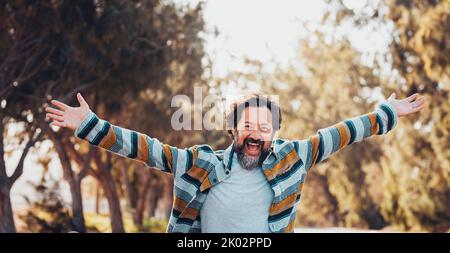 Crazy overjoyed adult man with arms outstretched smile and laugh alone in banner header image. Happiness and joyful people concept lifestyle. Trees and nature for outdoor leisure activity male Stock Photo