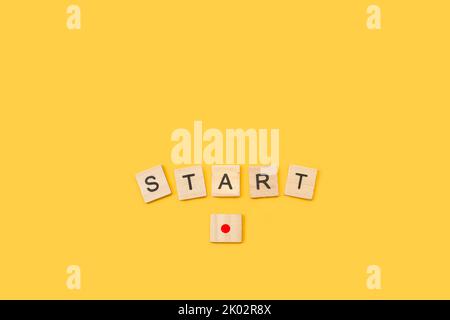 Start word write with wooden letter cubes and a block as a red button on yellow background Stock Photo