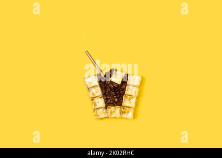 Ice cubes and coffee beans drinking glass shaped on a yellow background Stock Photo