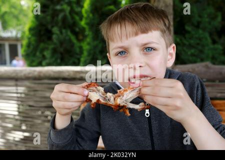 Boy has grilled chicken wings on restaurant terrace Stock Photo