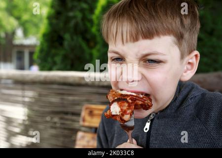 Kid eating grilled chicken wings on restaurant terrace Stock Photo