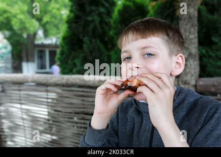 Kid has grilled chicken wings on restaurant terrace Stock Photo