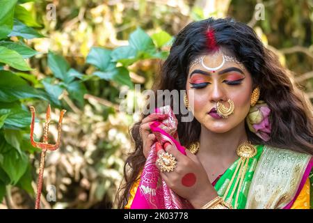 Concept Agomoni shoot with black haired Indian brunette  woman face with perfect makeup  and wearing jewelers with traditional dress like goddess . Stock Photo