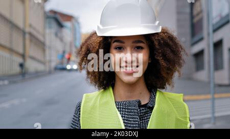 Female portrait worker profession close-up african american woman girl with curly hair civil engineer professional wearing safety helmet standing in Stock Photo