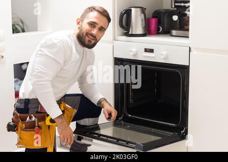 Young Male Technician Repairing Oven In Kitchen Stock Photo