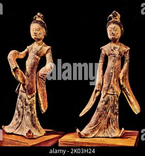 Six Dynasties pair of dancers have fashionable and flowing dresses, elaborately knotted hair coiffures, and they stand in dancing poses. They wear short, sleeveless outer vesist, which fit over the long and loose sleeved garments. They wear pointing shoe decorated with clouds decorated on the tips. Both dancers have their hands withdrawn into their sleeves. They confidently display their elegant faces, noble figures, and gracious dancing poses. A white case covers the black bisque, like white paper upon which red and black paints are applied. Stock Photo