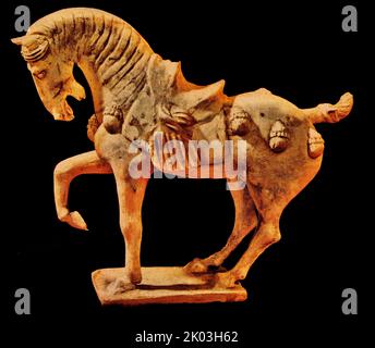 Tang Dynasty figurine of a horse. glazed white with traces of vermilion and ink painting. It stands upright on a rectangular platform. The horse is strong and has short legs and a large head in proportion. The head is straight, the eyes are open, the eyes are looking forward, the mouth is open and hissing, the sideburns are drooping to the left, the tail is upturned, and the limbs are stable. The eyes are drawn with vermilion and ink, and the lines of the muscles on the horse's face are very realistic. Stock Photo