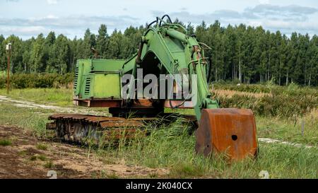 green excavator, green grass in the swamp on a very sunny day. Rusty chains and cup. Stock Photo