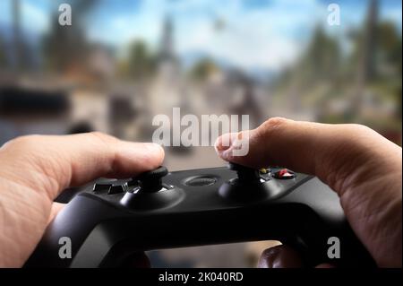 Video games. Modern joystick GAM22ICB in the hands of a gamer on the background of a video game on a large TV screen. Online games with friends, youth Stock Photo
