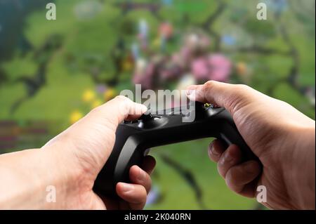 Against the background of a video game on a large TV screen, a joystick in the hands of a gamer. Modern technologies, GAM22ICB gamepad, video games, o Stock Photo