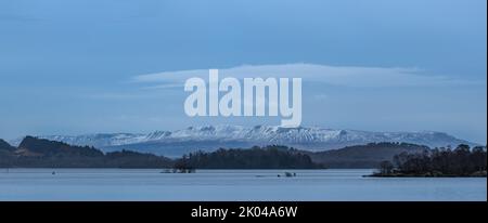 Stunning landscape image of Loch Lomond and snowcapped mountain range in distance viewed from small village of Luss Stock Photo