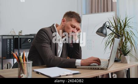 Bored sleepy business man worker working on laptop computer, yawning, leaning on hand falling asleep at office workplace. Exhausted tired freelancer workaholic man. Employment, occupation, workless Stock Photo