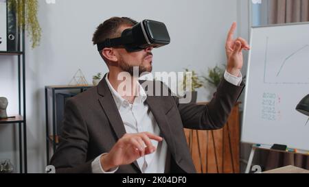 Businessman in suit working using virtual reality futuristic technology VR app headset helmet at home office. Freelancer man busy creating new architecture project. Remote education, study, learning Stock Photo