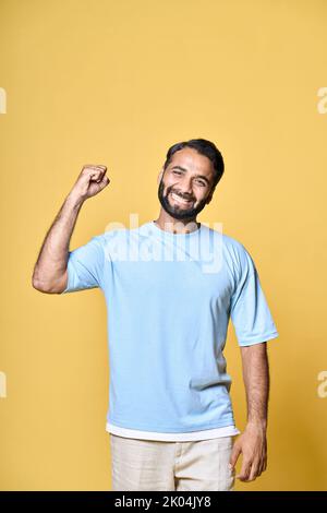 Happy indian man raising fist isolated on yellow background, vertical. Stock Photo
