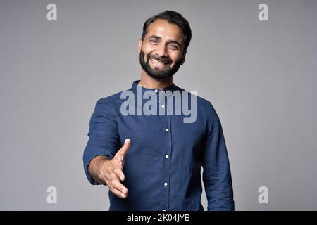Smiling indian business man extending hand for handshake isolated on gray. Stock Photo