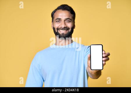 Happy indian man showing mobile phone pointing at screen isolated on yellow. Stock Photo