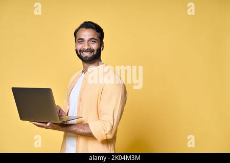 Happy indian business man student holding laptop isolated on yellow. Stock Photo