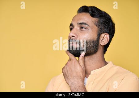 Thoughtful doubtful indian man thinking isolated on yellow. Portrait Stock Photo