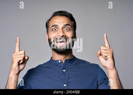Happy surprised indian business man pointing fingers up isolated on gray. Stock Photo