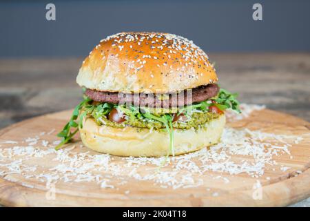 Vegan hamburger with no meat alternative. Plant based burger with pesto, vegan cheese and organic cherry tomatoes. Street fast food. Homemade bun. Stock Photo