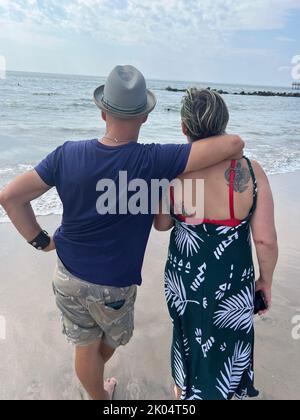 Couple on the sand looking out at the Atlantic Ocean at Coney Island, Brooklyn, New York. Stock Photo