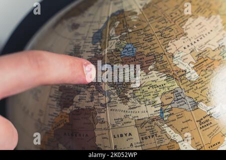 Close-up human finger pointing at a spot on a spinning geographical physical globe. Earth model on a stand. High quality photo Stock Photo