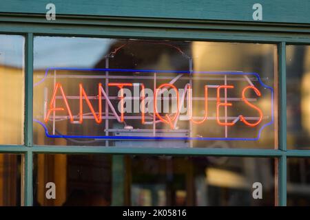 Shop window neon sign spelling antiques in red with green wood window frame and edge Stock Photo