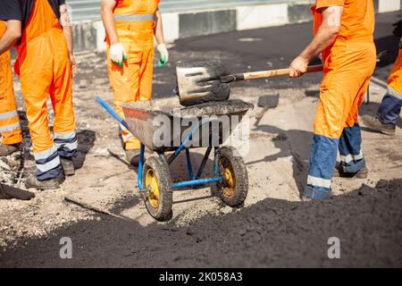 Repair of road. Laying asphalt on road. Worker in orange clothes. Builders in summer in city. Stock Photo