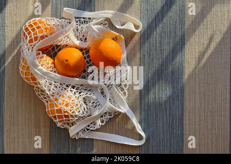 Mesh bag with oranges in natural sunlight, top view Stock Photo