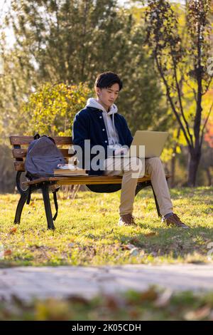 Happy Chinese college student using laptop on campus Stock Photo