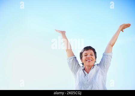 Playful female enjoying freedom. Low angle view of playful mature woman enjoying freedom against sky with hands outstretched. Stock Photo