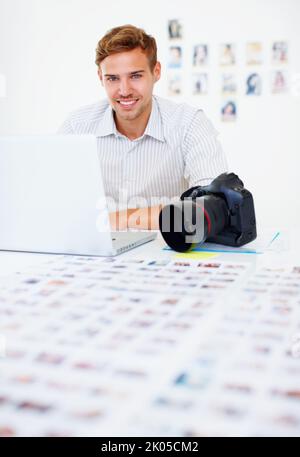 Smart photographer using laptop. Portrait of smart male photographer using laptop and smiling. Stock Photo