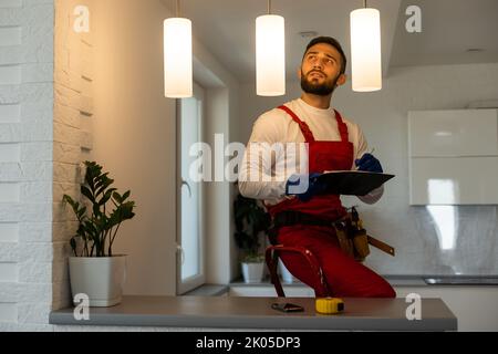 Installation lighting. Builder is holding a tablet in his hands. Concept - lighting engineer. Process installing. Electrician Stock Photo