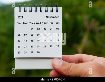 Hand holding November 2022 calendar with copy space and nature background. Stock Photo