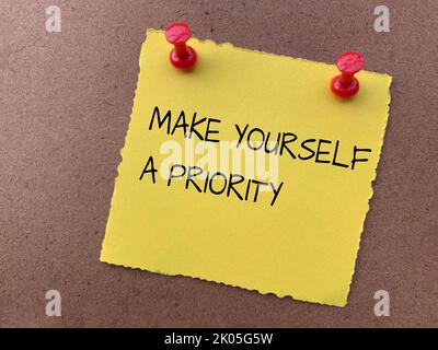 Make yourself a priority text on yellow notepad with wooden background. Motivational concept. Stock Photo