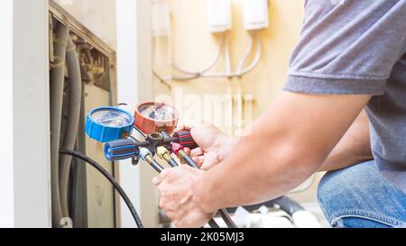 Air repair mechanic using measuring equipment for filling industrial factory air conditioners. Stock Photo