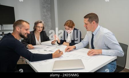 Four colleagues are discussing blueprints in a conference room in an office. Brainstorming of engineers and architects. Stock Photo