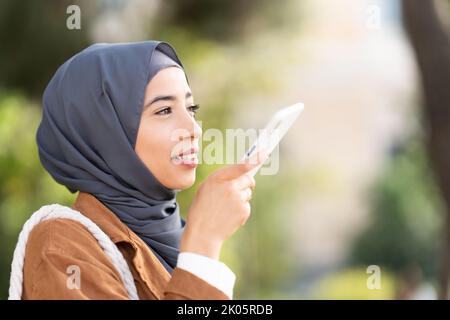 Muslim woman sending a voice message outdoors Stock Photo